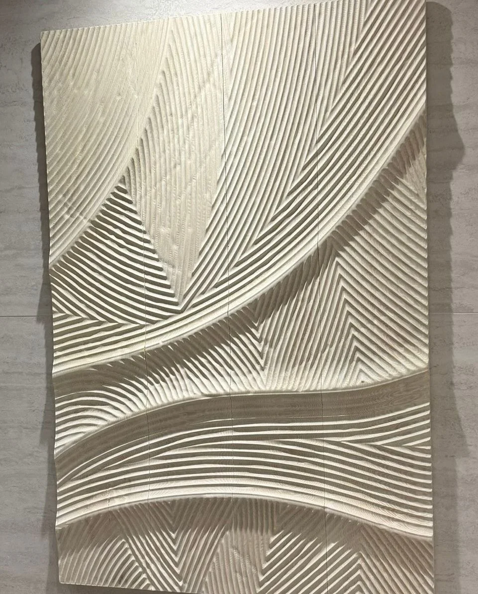 A white carved wood wall panel with sweeping wave relief, installed on a pale stone-textured wall.