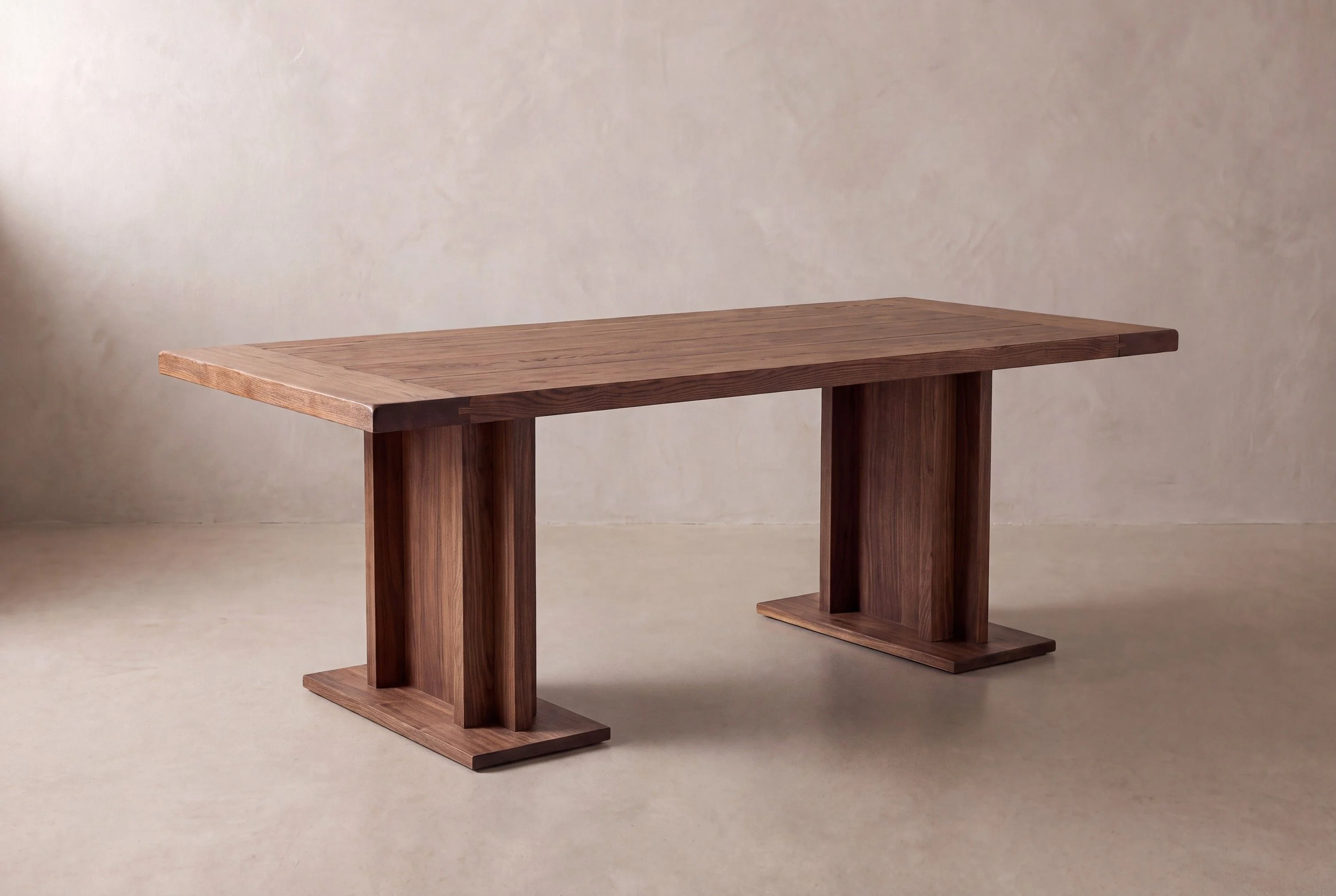 A rendering of a walnut dining table on two plank pedestals in a limewash studio.