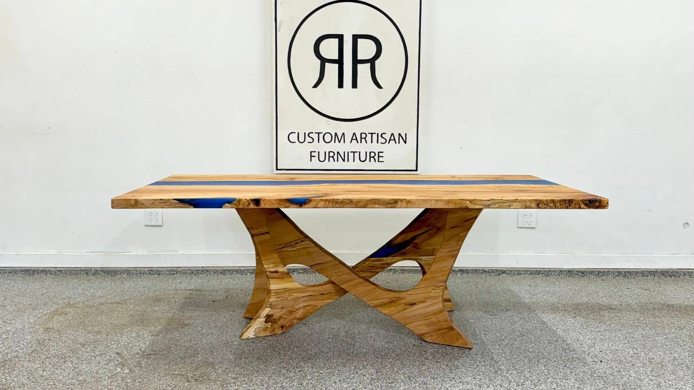 A table on a sculptural base of two shaped wooden legs that cross beneath a top with a blue resin channel.