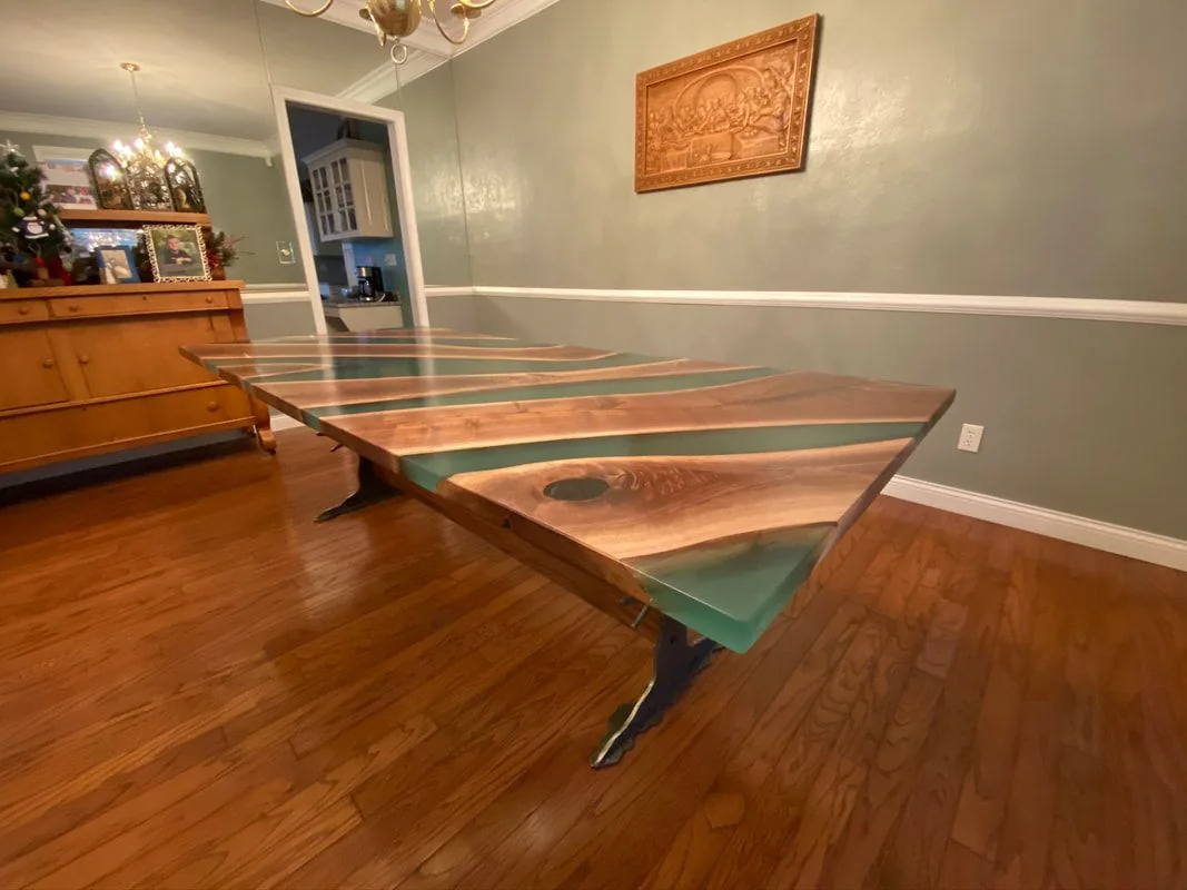 Custom wood and green resin dining table in room with hardwood floors, chandelier, and carved wall art.