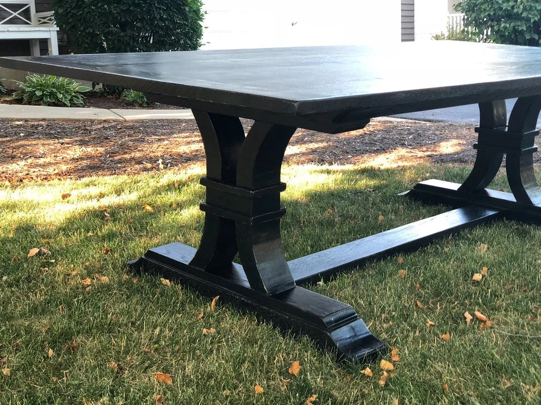 Black wooden table with rectangular top and curved legs connected by a horizontal beam, photographed against a dark studio wall.