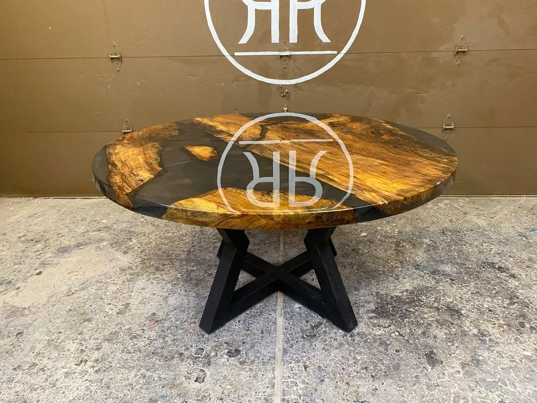 Round wooden table with black resin inlay and an X-shaped black base, photographed against a dark studio wall.