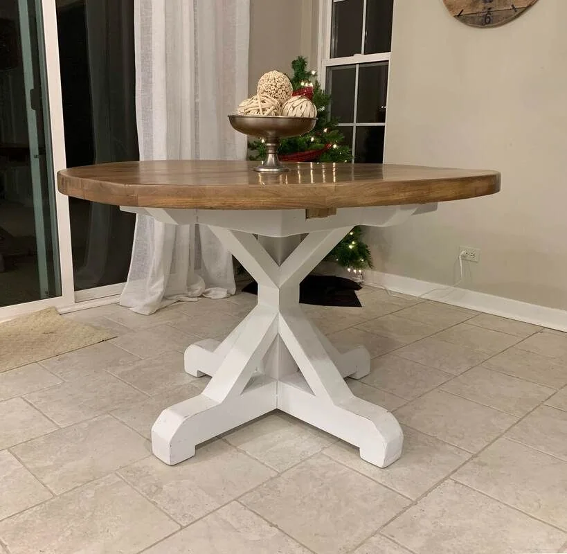 A thick natural wood table on white ornate pedestal legs, paired with a matching built-in white bench, photographed against a dark studio wall.