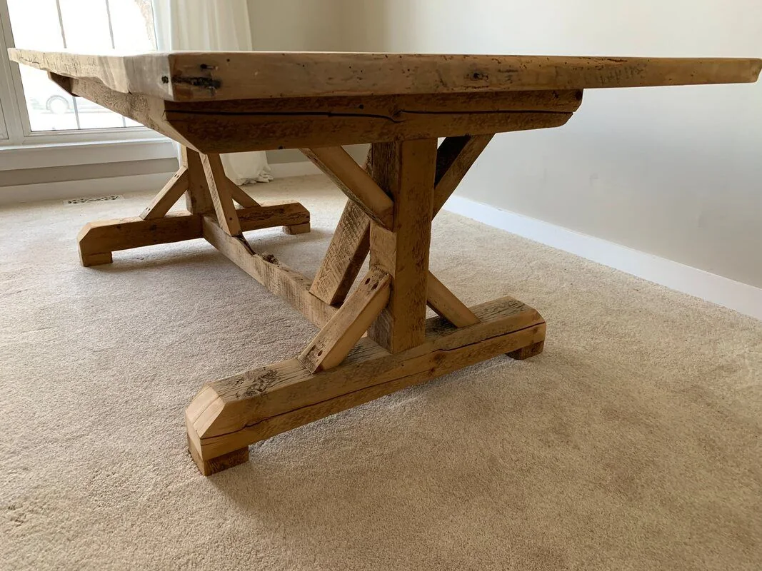 Rustic wooden table with a thick top and trestle-style legs on beige carpet in a bright room