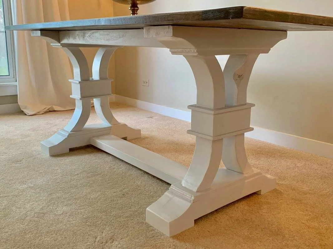 Wooden table with white curved legs and decorative square blocks, placed on beige carpet in a light-colored room.