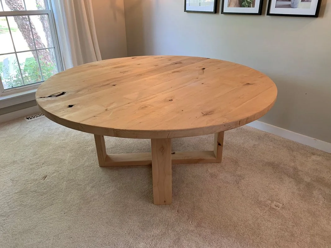 Round rustic wood table with intersecting square base, photographed against a dark studio wall.