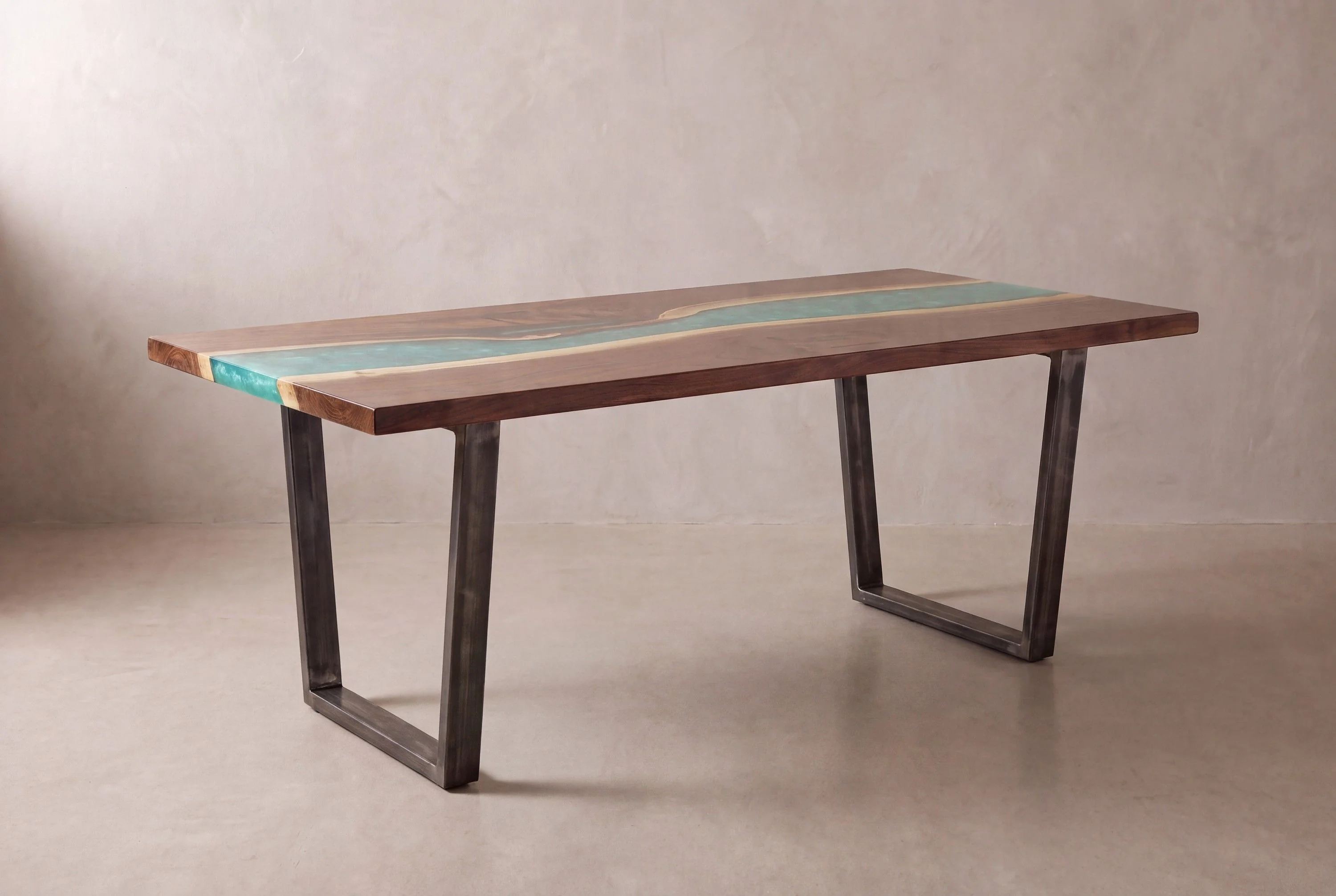 A rendering of a long walnut table with a wide turquoise resin river on raw steel trapezoid legs, in a limewash studio.