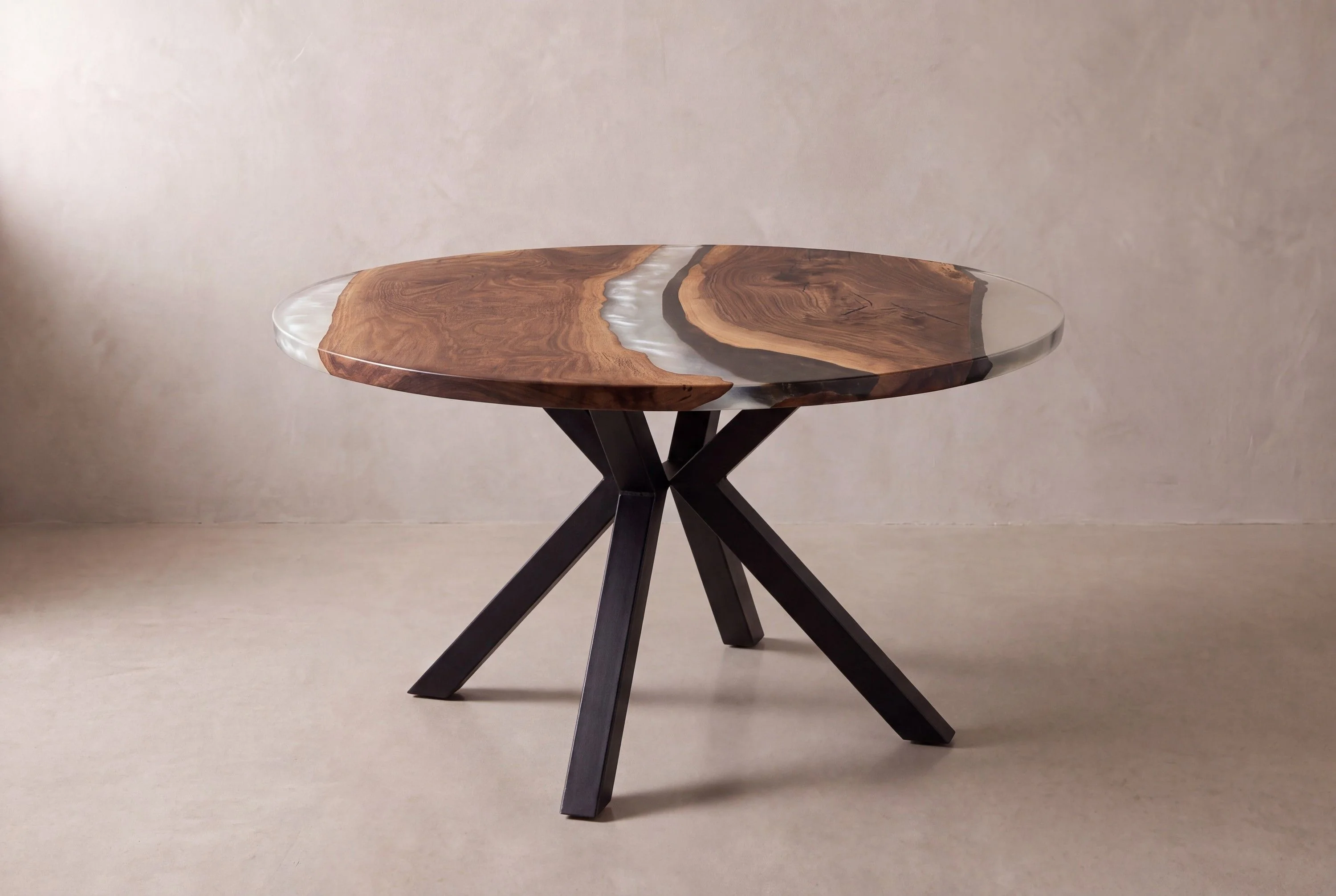 A rendering of a round walnut table with a clear and dark resin band, on a black steel base with splayed legs, in a limewash studio.