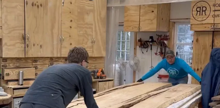 Woodworkers moving large hardwood slabs for a custom wood and epoxy dining table handcrafted in Geneva, Illinois.