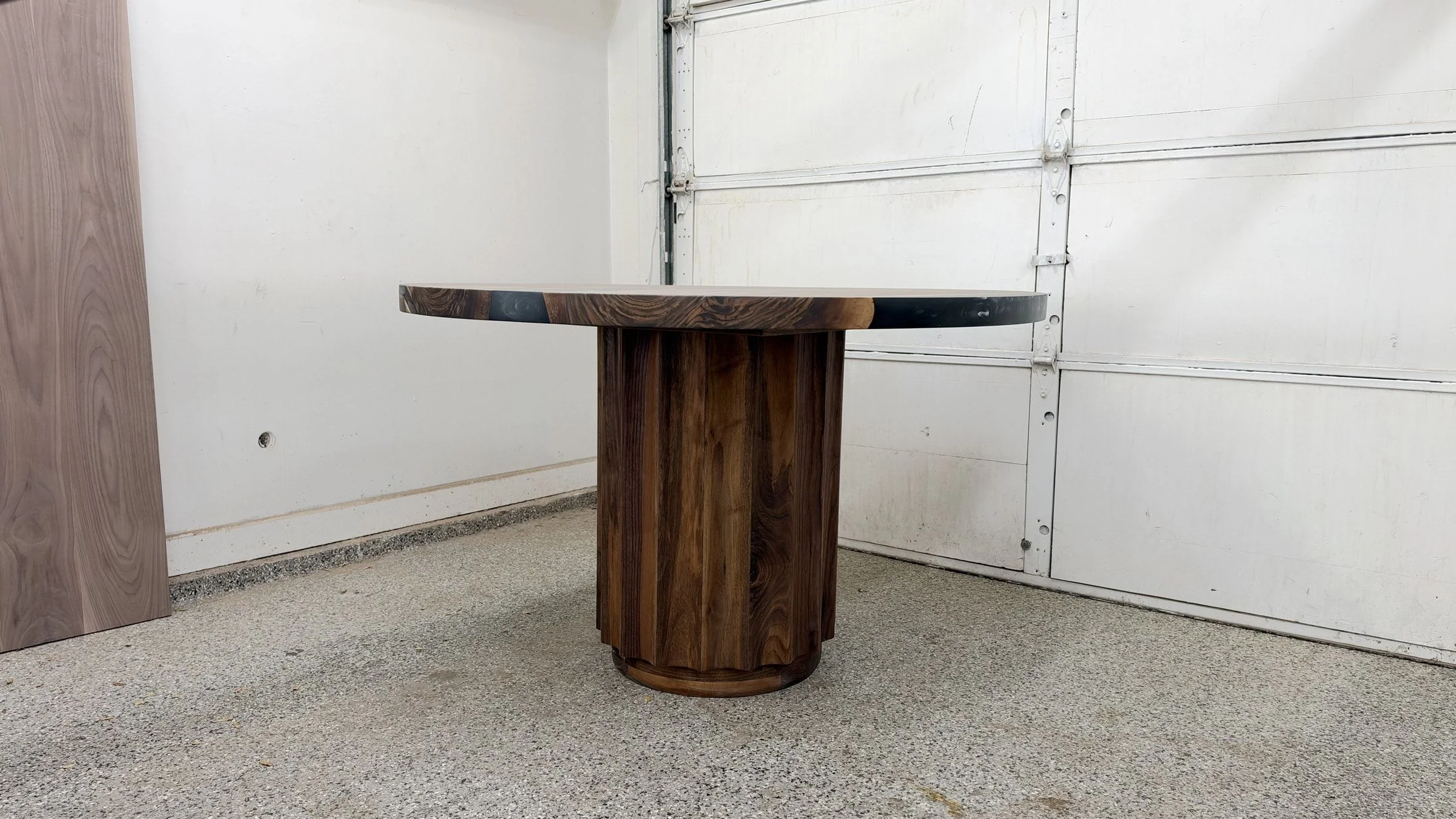 Round black river table at eye level, showing the edge of the top and the fluted walnut drum pedestal.