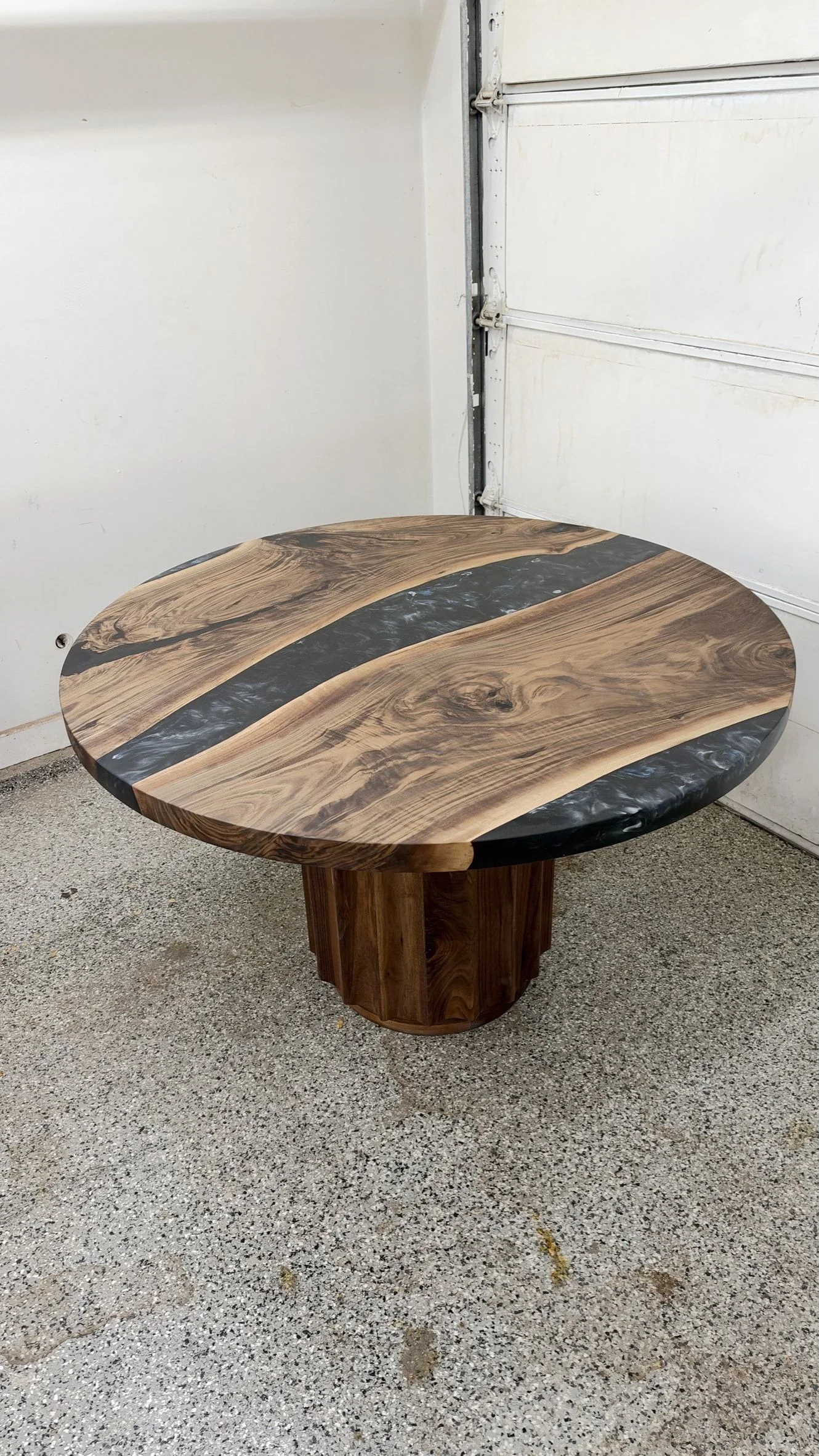 Round black river table from above and to one side, with the resin river running across the top and the fluted pedestal below.