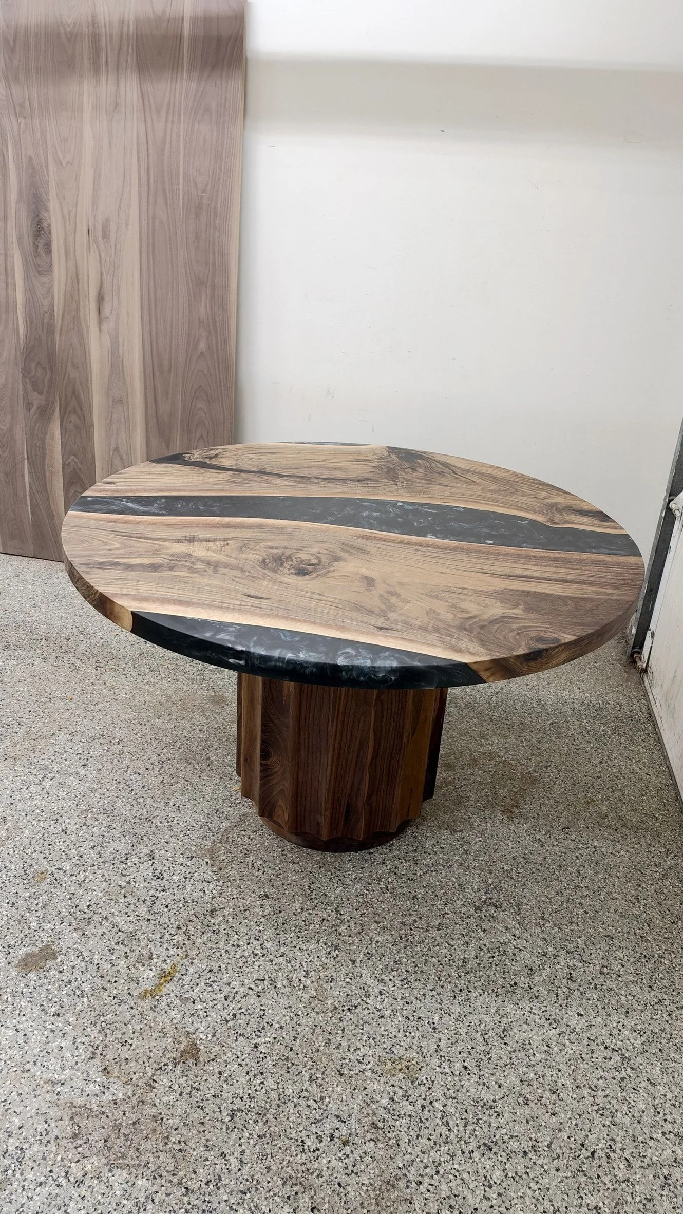 Round black river table from a low angle across the floor, with the fluted pedestal under the round top.