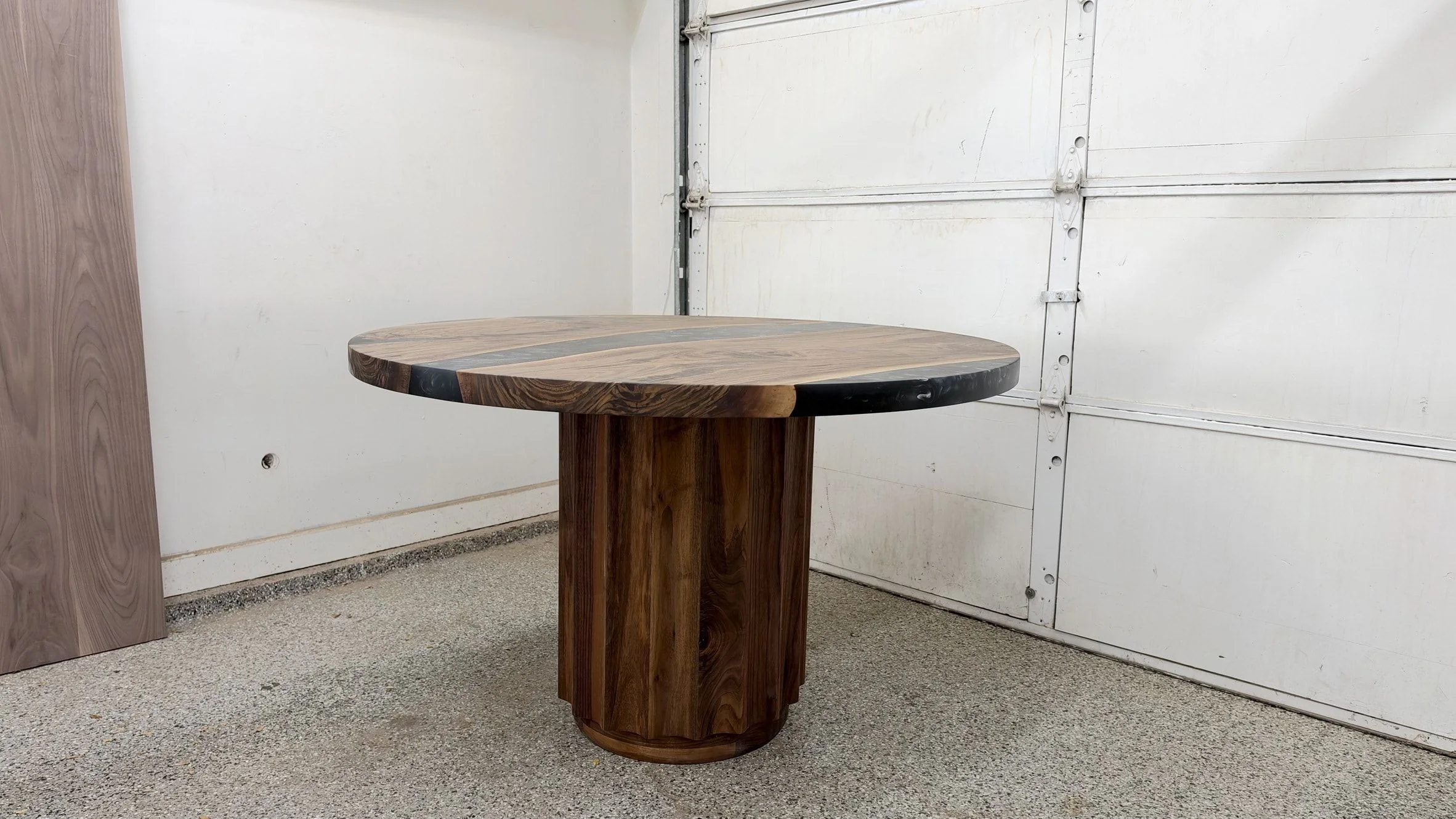 Round black river table seen from the side, showing the thin edge of the top and the full height of the fluted drum pedestal.