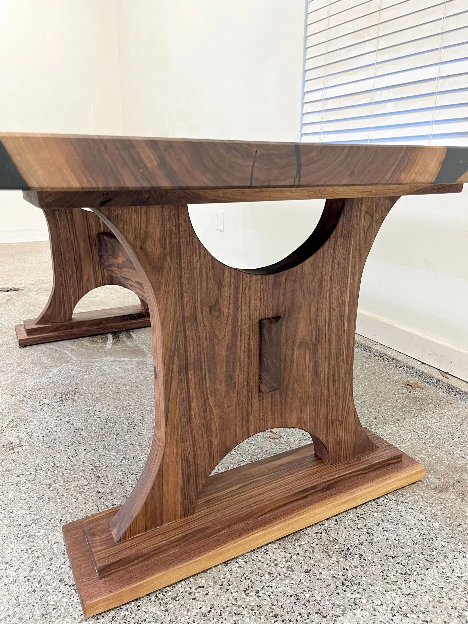 The arched walnut trestle base seen from the end, showing the curve of the cut-out and the stepped foot.