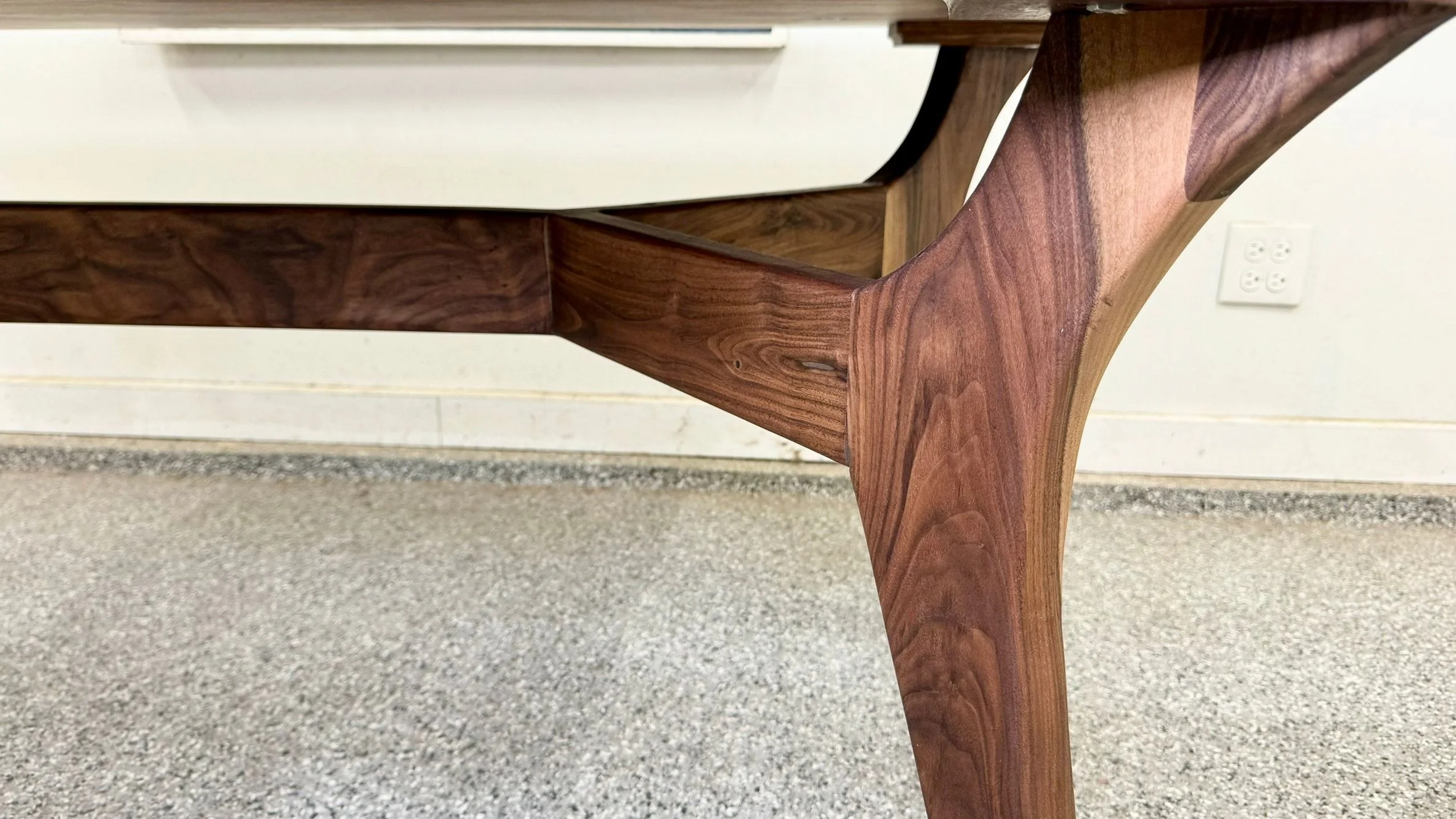 Close view of a splayed walnut leg meeting the rail of a table.