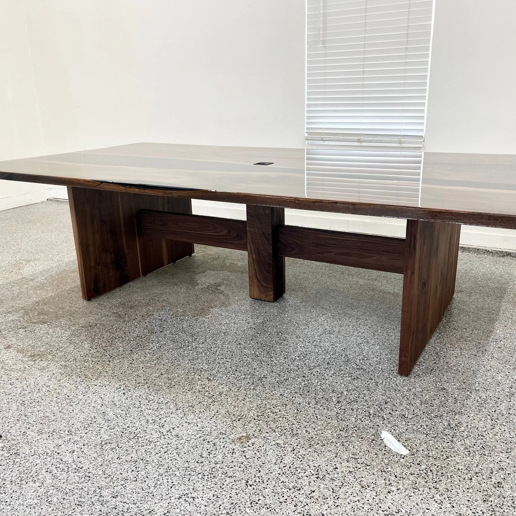 A long walnut conference table on slab legs joined by a stretcher, with a power grommet in the top.