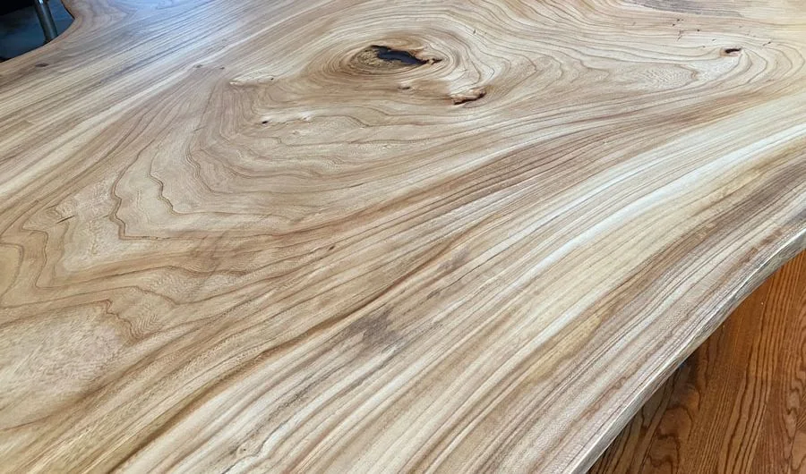 Large polished live edge wood table with intricate natural grain patterns and smooth finish, showcasing artisanal woodworking.