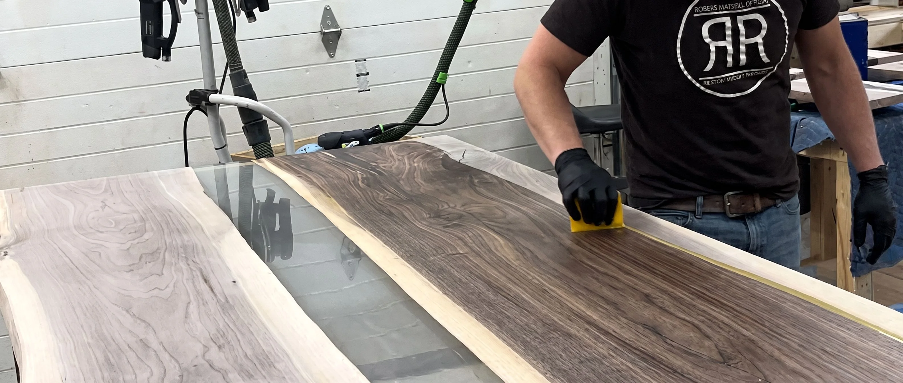 Gloved hands drawing a coat of sealer down the surface of a finished walnut river top.