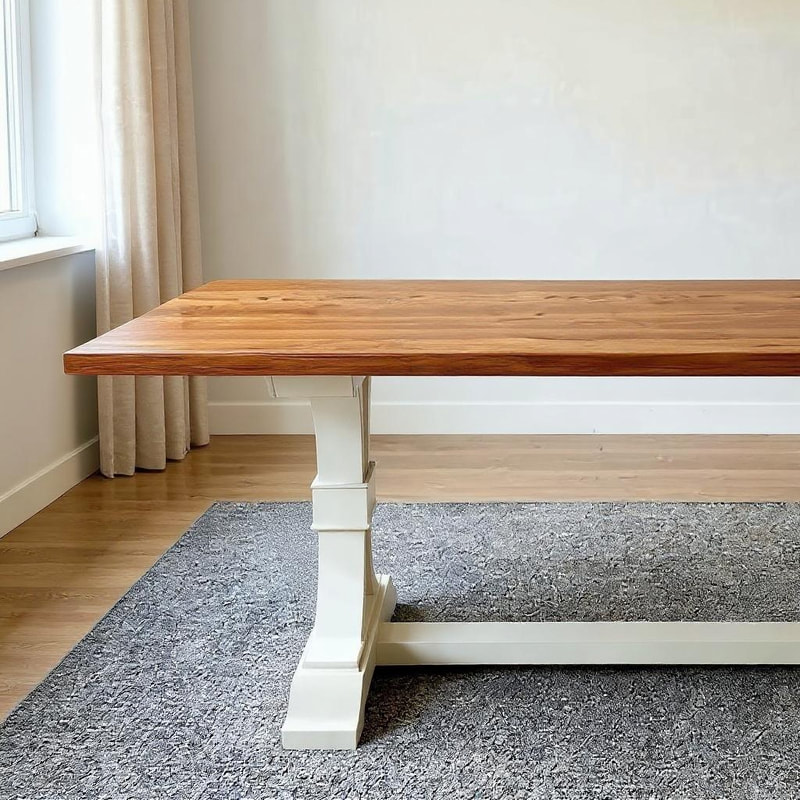 Elegant wooden table with a natural wood top and light-colored base, positioned on a gray rug in a sunlit room with beige curtains, light walls, and wooden flooring.