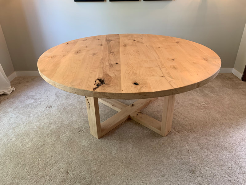 Round rustic wood table with Open Loop base on carpeted floor in bright room.