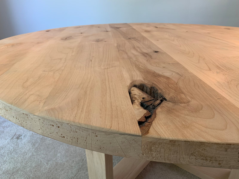 Close-up of round wood table with natural grain and knot detail, smooth edges, and sturdy legs.